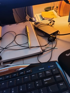 Decorative photo of a messy desk showing keyboard, notebook, pen and earbuds.